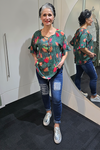 Woman standing in front of a mirror wearing a colorful shirt and blue jeans. Tie Neck Top Green