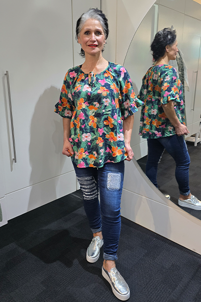 Woman wearing a colorful floral blouse and jeans standing in front of a mirror. Tie Neck Top Navy