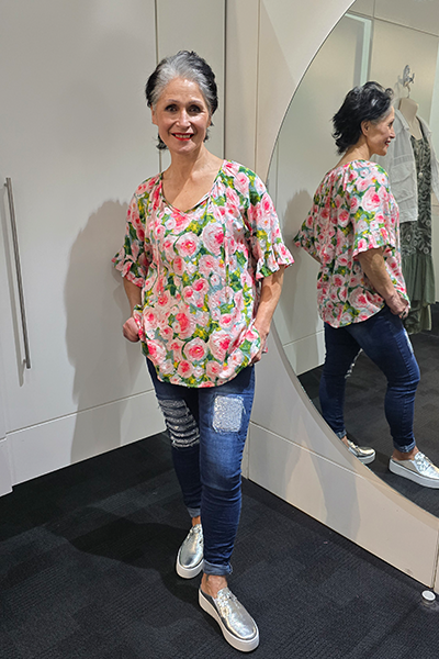 Woman wearing a floral top and jeans standing in front of a mirror. Tie Neck Top Pink