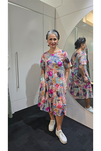 Woman wearing a colorful floral dress standing in front of a mirror. Tiered Dress Multi