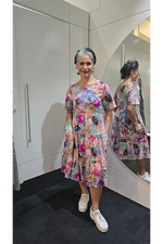 Woman wearing a colorful floral dress standing in front of a mirror. Tiered Dress Multi