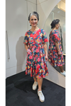Woman wearing a colorful floral dress standing in front of a mirror. Tiered Dress Red
