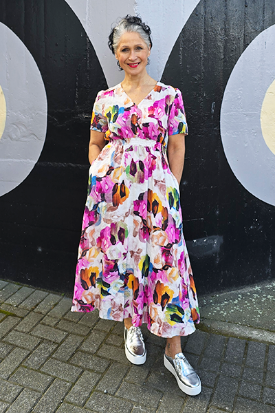 Woman wearing a colorful floral dress standing in front of a black and white wall.
V Neck Dress Pink