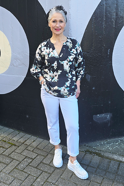 Woman in floral blouse and white pants standing in front of a black and gray wall.
V Neck Top Black