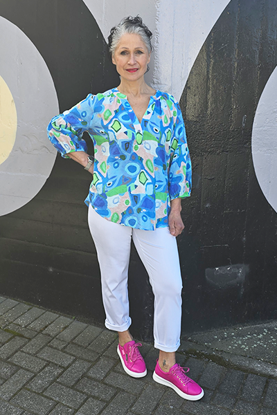 Woman wearing a colorful floral blouse and white pants standing against a black and white circular wall.
V Neck Top Blue
