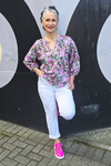 Woman in a floral blouse and white pants standing against a black and gray background
V Neck Top Purple