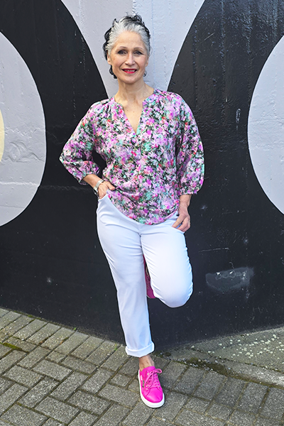 Woman in a floral blouse and white pants standing against a black and gray background
V Neck Top Purple