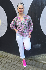 Woman in a floral blouse and white pants standing against a black and gray background
V Neck Top Purple