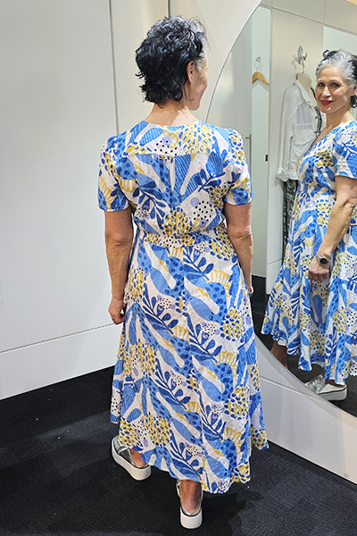 Woman trying on a blue and yellow patterned dress in front of a mirror.
V Neck Dress Blue