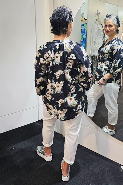 Person wearing a black floral shirt and white pants standing in front of a mirror.
V Neck Top Black
