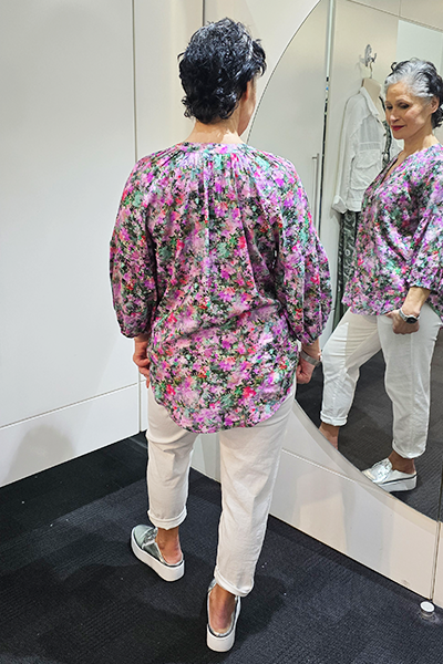 Person wearing a floral blouse and white pants standing in front of a mirror.
V Neck Top Purple