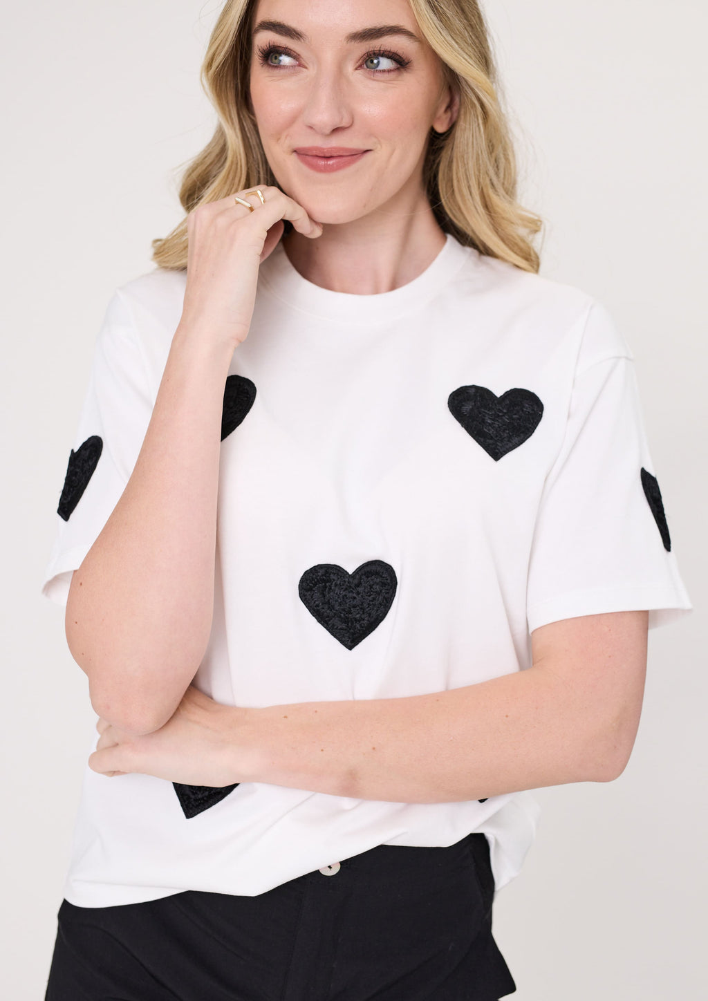 Woman wearing a white t-shirt with black heart patterns on a plain background
Valentina Tee White
