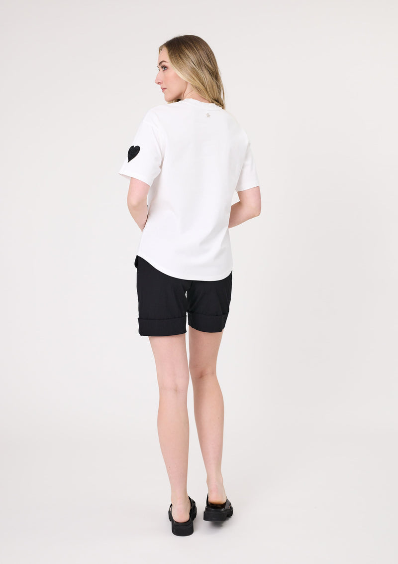 Woman wearing a white t-shirt with a black heart design and black shorts on a white background
Valentina Tee White