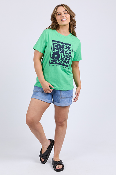Woman wearing a green t-shirt with a blue graphic design on a white 
Winona Tee Spring Greenbackground