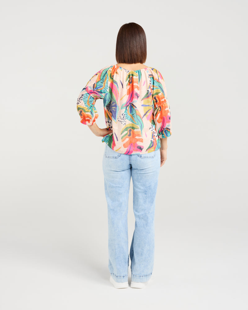 Woman wearing a colorful floral blouse and light blue jeans on a white background
Caitlin Top Vivid