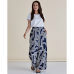 Woman wearing a white top and blue patterned pants against a beige background