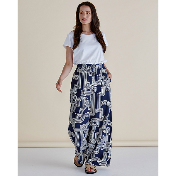 Woman wearing a white top and blue patterned pants against a beige background