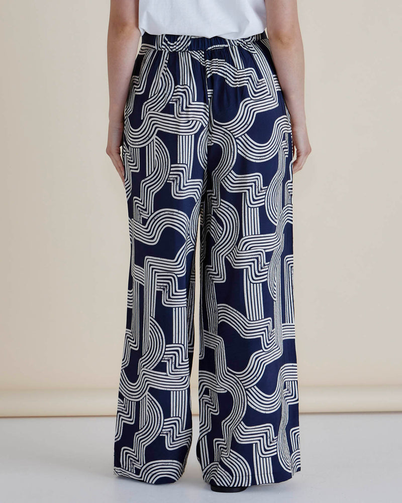Navy blue pants with white geometric pattern worn by a person on a beige background