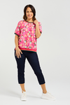 Woman wearing a pink floral top and dark pants on a white background Zoe Top Petal Confetti