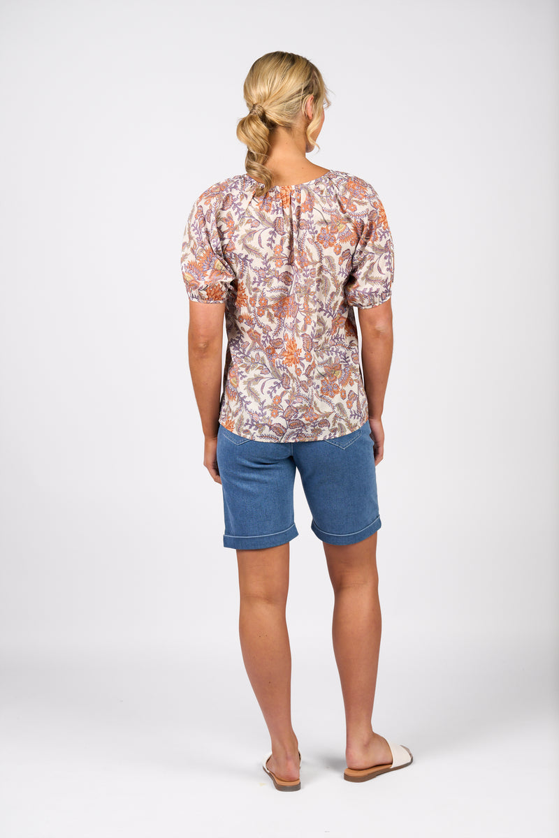 Woman wearing a patterned top and blue shorts on a white background